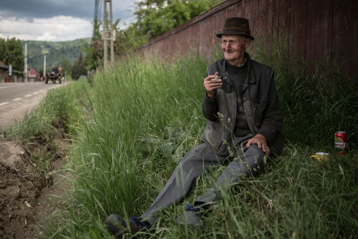 A hetvenéves Miklós a fűben ülve dohányzik gyimesbükki háza közelében 2021 júniusában | fotó: Szöllősy Mátyás