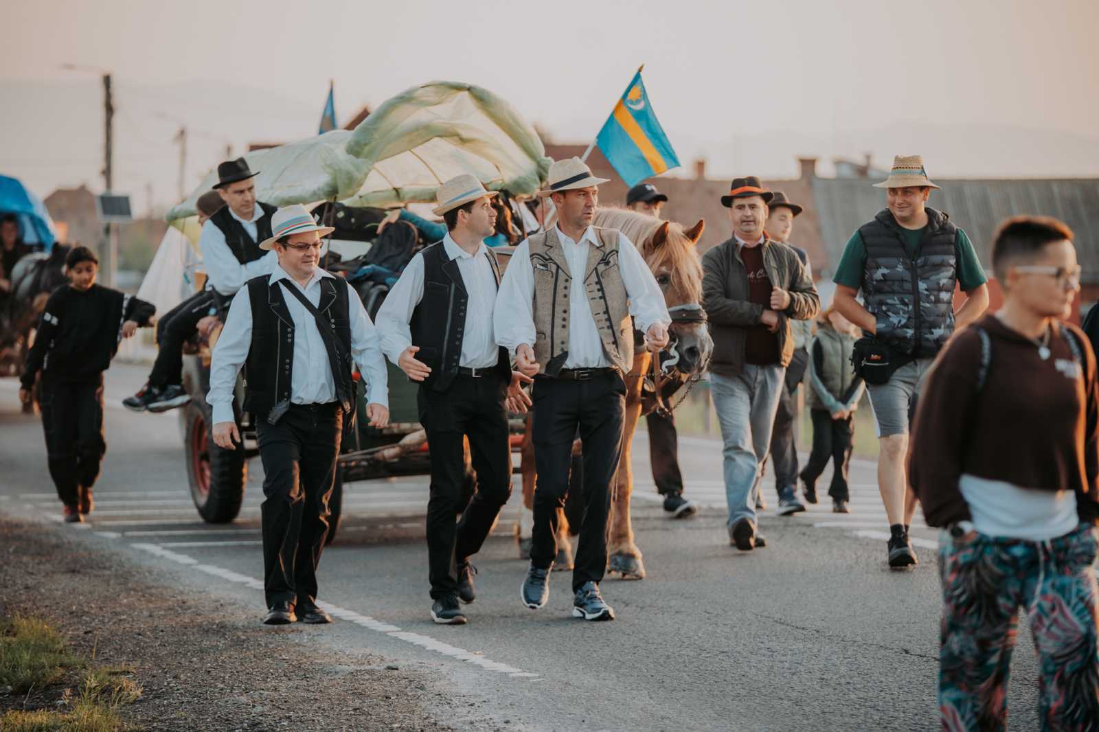 Még harmatos volt a fű, de a zarándokok már rég úton voltak. Székely zászló leng a lágy szélben, népviseletbe öltözött fiatalok és idősek haladnak csendesen, néha énekelve, néha csak magukba mélyedve. Mögöttük a nap első sugarai festik aranyra az ég alját – mintha az ég is áldását adná az útra.