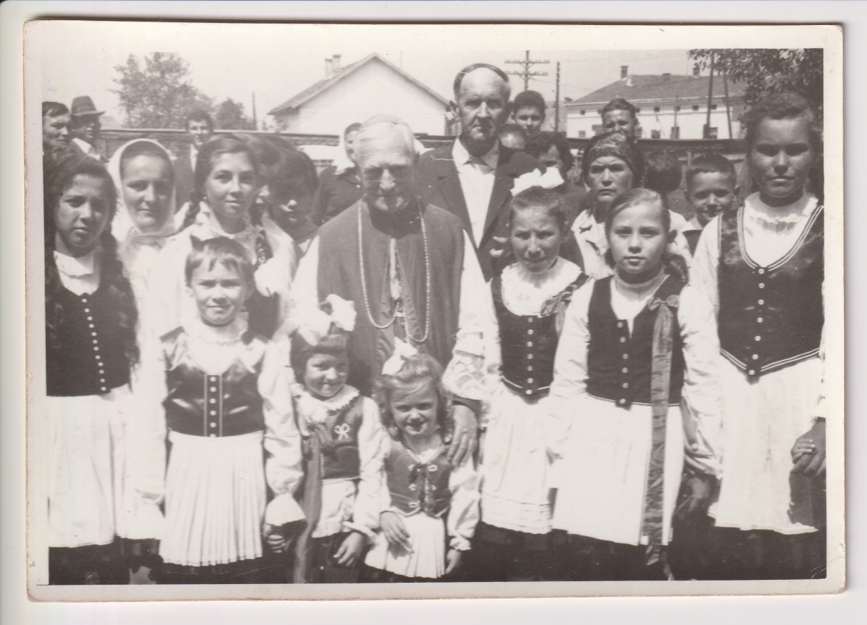 Márton Áron 1969-es bérmaútja alkalmával a gyergyóalfalvi plébánia udvarán, székelyruhás kislányok körében.