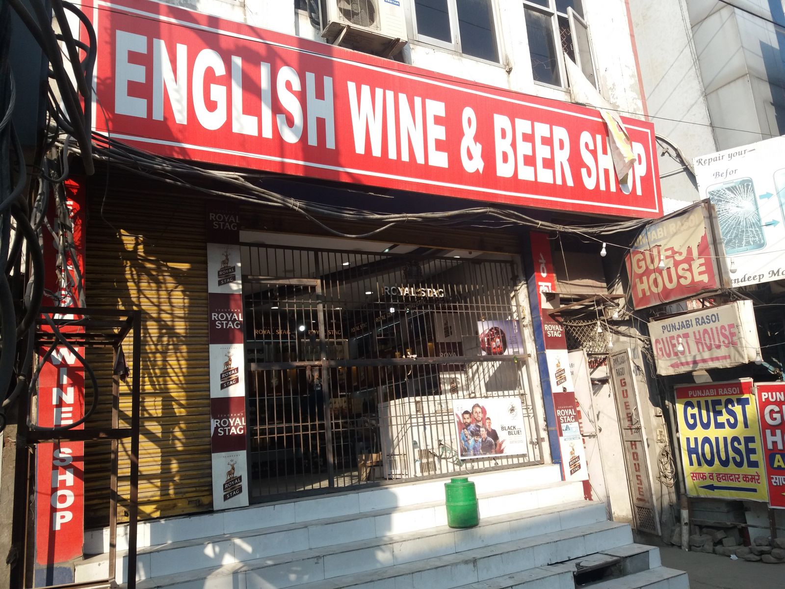 Borszaküzlet bor nélkül. India lakosságának 95 százaléka olyan hitrendszer követője, mely tiltja az alkoholfogyasztást, ez közös vonás a hinduizmusban, az iszlámban és a szikh vallásban. Ennek ellenére a szeszipar minden bizonnyal virágzik, legalábbis a kizárólag alkoholos italokat forgalmazó boltok tekintélyes számából erre lehet következtetni. Ezeket általában az Angol sör és bor üzlet név alatt futnak, ami elég megtévesztő elnevezés, két okból is. Egyrészt bort alig tartanak, olyat is láttam, amelyikben egyáltalán nem volt, whiskys üvegekkel ellenben tele vannak a polcok. Másrészt az angoloknak semmi közük az egészhez, ha csak az nem, hogy az indaiak a gyarmati időkben kaptak rá a whiskyre.
