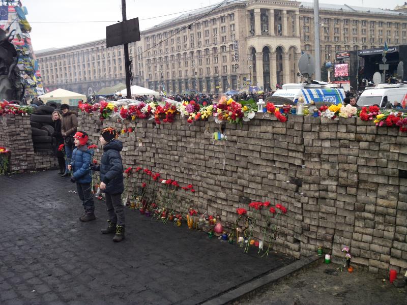 Kockakőből rakott védőfal, előtte és rajta az áldozatok emlékére elhelyezett virágok, mécsesek