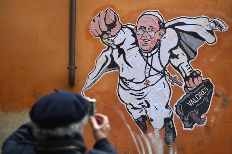 2014. január 29. - Rómában bukkant fel egy Ferenc pápát szuperhősként ábrázoló graffiti, amelyet a Vatikán hivatalos Twitter-oldalán osztottak meg: mosolyogva, jobb karját előrenyújtva pózolt egy ház falán, bal kezében pedig híres fekete táskáját szorítot